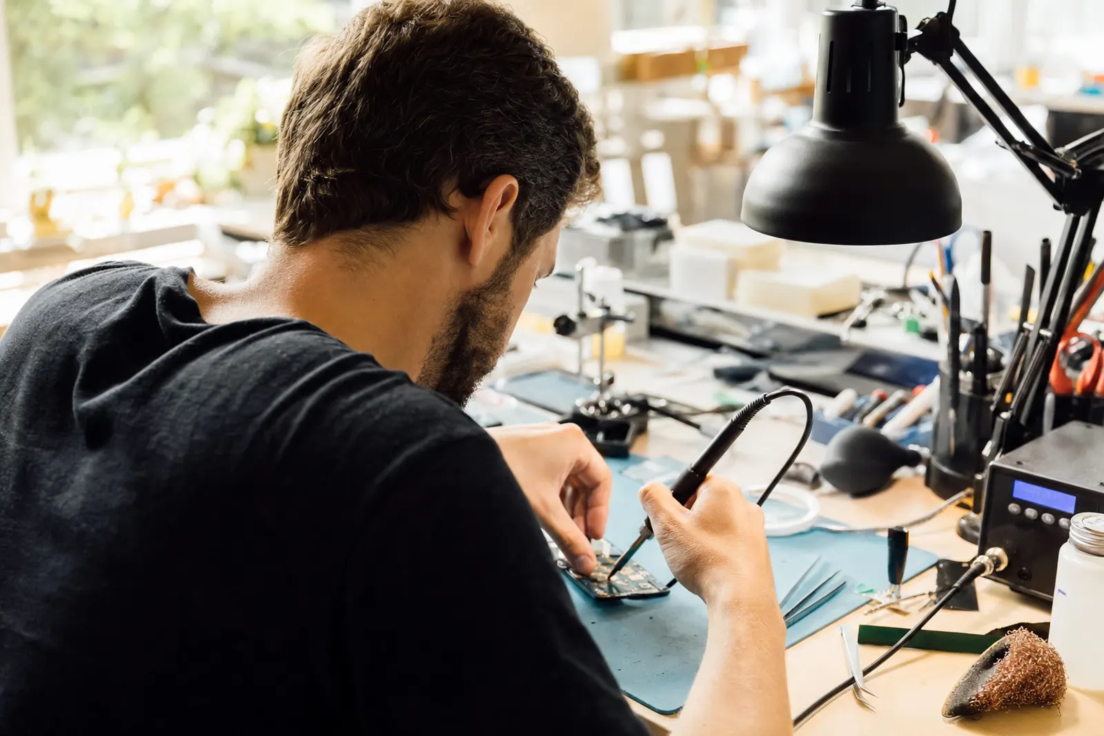 Techniker arbeitet konzentriert mit dem Lötkolben an einer Platine an seiner Werkbank